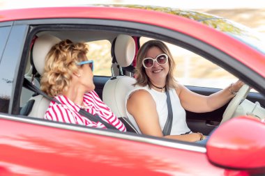 Kiralık kırmızı bir arabayla seyahat eden iki arkadaş, gülüyorlar ve tatillerinin tadını çıkarıyorlar.