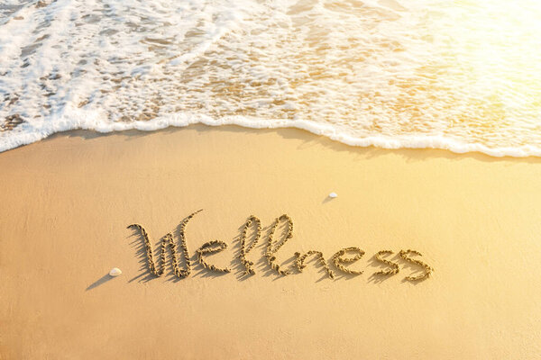 Word "wellness" written on the sand of the beach. Positive message written on the seashore at sunset