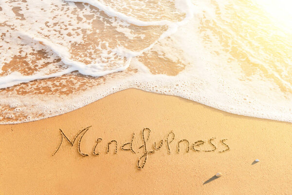 Слово "Mindfullness" написано на песке пляжа. Позитивное послание на берегу моря на закате