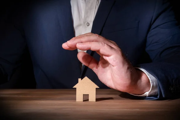 Insurance professional covering a cardboard cut-out house with his hand. Home and fire insurance. Protection against unforeseen events at home