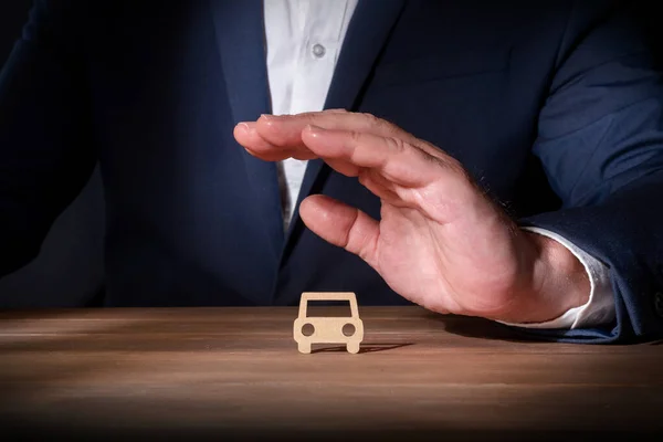 Insurance professional covering a cardboard cut-out car with his hand. Fully comprehensive vehicle insurance. Protection against unforeseen events on the road