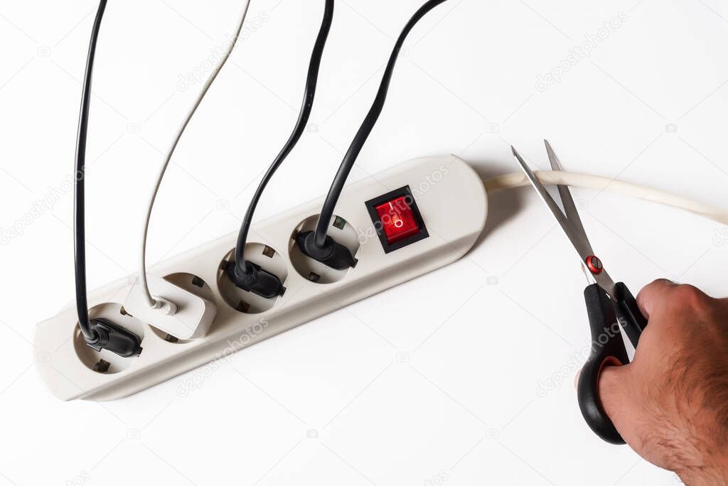 Multi-plug power strip with many devices connected and one hand cutting the cable. Concept of power restriction and power outages