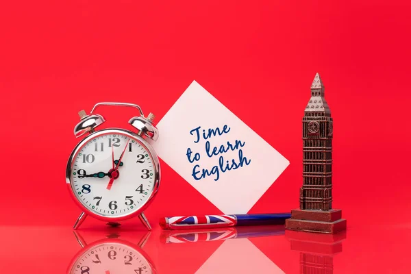 Time to learn English. Pen with the flag of the United Kingdom on red background next to a clock and a card to write messages. Study a new language