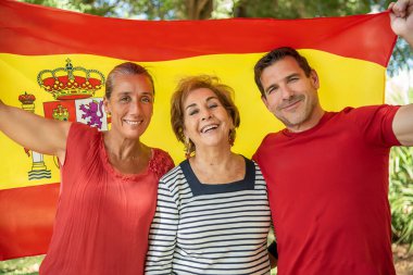 Orta yaşlı bir oğlan ve yaşlı bir bayanın yanında orta yaşlı bir kız İspanya 'nın kırmızı ve sarı bayrağını göndere çekiyor. İspanyol olmaktan gurur duyuyorum. Çok yaşa İspanya