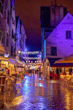 Plumereau Meydanı, yağmurda yılbaşı aydınlatmalarıyla süslenmiş yarı keresteli evlerden inşa edilmiş ortaçağ mimarisi. Ön plandaki ıslak kaldırım taşlarına odaklanmış. Tur, Fransa.