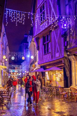 Tur sakinleri, yağmurda yılbaşı aydınlatmalarıyla dekore edilmiş yarı ahşap evlerden inşa edilmiş ortaçağ mimarisi meydanı Place Plumereau 'daki barlarda dinleniyor. Tur, Fransa. 27 Kasım 2021