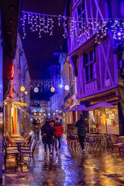 Tur sakinleri, yağmurda yılbaşı aydınlatmalarıyla dekore edilmiş yarı ahşap evlerden inşa edilmiş ortaçağ mimarisi meydanı Place Plumereau 'daki barlarda dinleniyor. Tur, Fransa. 27 Kasım 2021