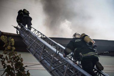 Oksijen maskeli merdivenlerdeki itfaiyeciler şehrin ortasındaki eski bir evde çıkan yangını söndürüyor.