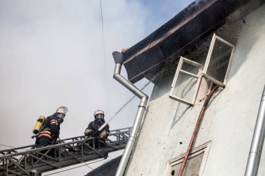 Oksijen maskeli merdivenlerdeki itfaiyeciler şehrin ortasındaki eski bir evde çıkan yangını söndürüyor.