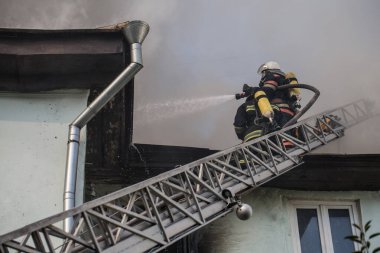 Oksijen maskeli merdivenlerdeki itfaiyeciler şehrin ortasındaki eski bir evde çıkan yangını söndürüyor.