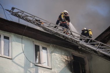 Oksijen maskeli merdivenlerdeki itfaiyeciler şehrin ortasındaki eski bir evde çıkan yangını söndürüyor.