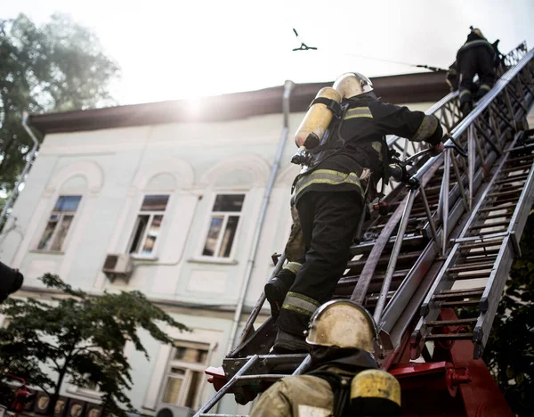 身着氧气面罩的消防员在梯子上扑灭了市中心一幢老房子的大火 — 图库照片