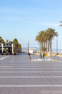 VALENCIA, İspanya - 17 Nisan 2021: Malvarrosa 'nın güneşli sonbahar plajında yaz atmosferi. Deniz kıyısındaki küçük restoranlar tatilcileri dinlenmek için güneşli teraslara çekiyor..