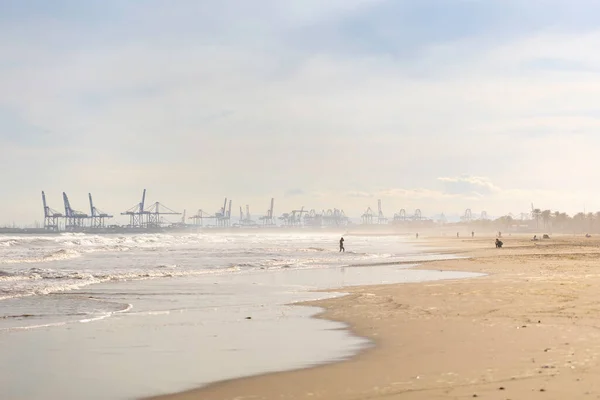 Summer vibes on the sunny autumn beach of Malvarrosa in Valencia, Spain. Vast expanses of smooth fine sand on the sea coast attract vacationers to solitary walks along the bubbling foamy waves.