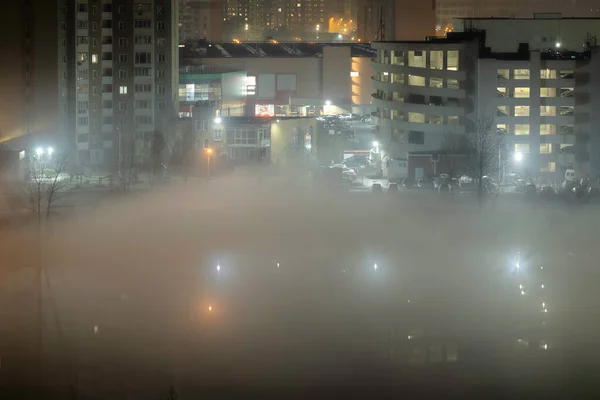 Night cityscape of the big city. Awesome bright, multi colored light in thick fog at empty streets. Apartment buildings in bedroom community, commuter town area. Darnytsia, Kyiv. Ukraine. 2021