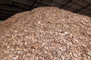 piles of hardwood wood chips are stored under the canopy as solid fuel