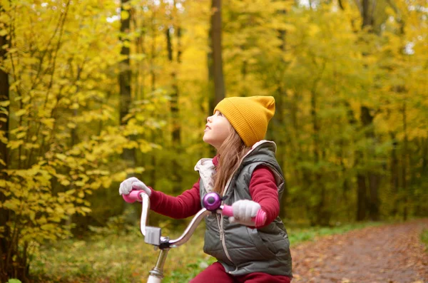 Gülümseyen bir kız sonbahar parkında bisiklet sürüyor.