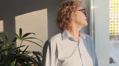  Olgun orta yaşlı kadın ofiste dikilip pencereye bakıyor.