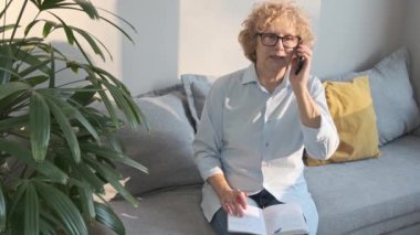 Gülümseyen, kendine güvenen olgun, orta yaşlı bir kadın koltukta oturuyor.
