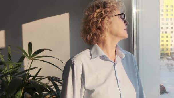 Ώριμη μεσήλικη γυναίκα στέκεται στο γραφείο στο σπίτι και κοιτάζοντας το παράθυρο — Αρχείο Βίντεο