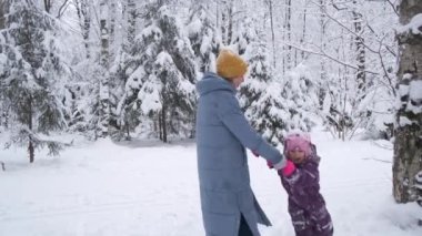 Beautiful senior woman is spinning with her granddaughter in the snow forest.