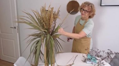 Sarı önlüklü yaşlı kadın portresi. Kurumuş çiçek ve otları düzenliyor.