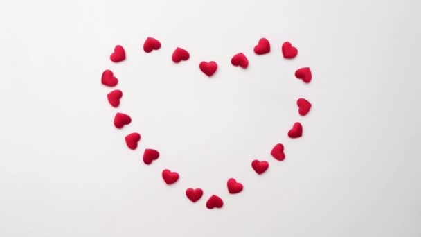 Corazón hecho de pequeños corazones decorativos rojos brillantes que aparecen sobre un fondo blanco con manos de niño — Vídeos de Stock