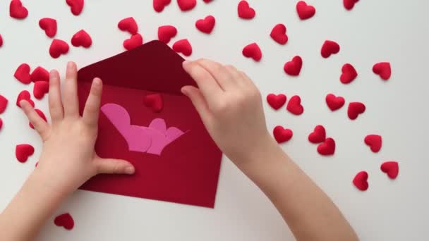 Kinderhände stecken Valentinsherzen in roten Umschlag — Stockvideo