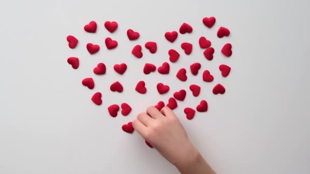 Cuore fatto di rosso lucido piccoli cuori decorativi su uno sfondo bianco con mano bambino — Video Stock