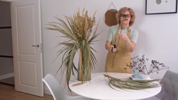 Портрет старшої жінки в жовтому фартуху, що влаштовує сушені квіти і трави — стокове відео