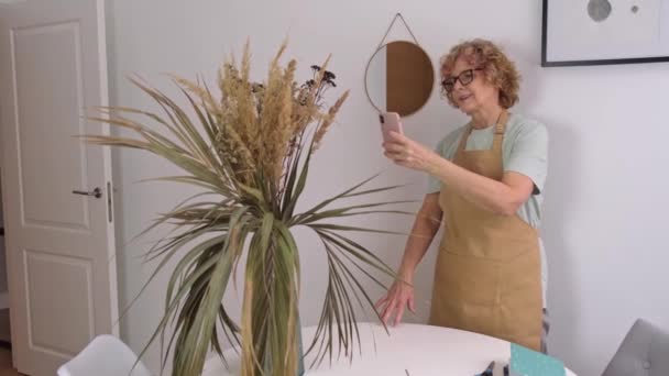 Porträt einer Seniorin in gelber Schürze fotografiert getrocknete Blumen und Kräuter — Stockvideo