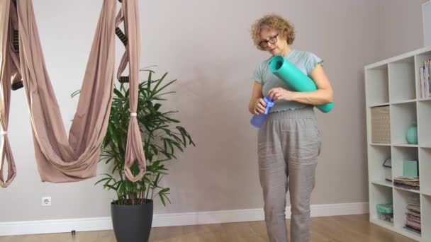 Senior hermosa mujer deportiva con gafas que sostienen la estera para el yoga — Vídeos de Stock