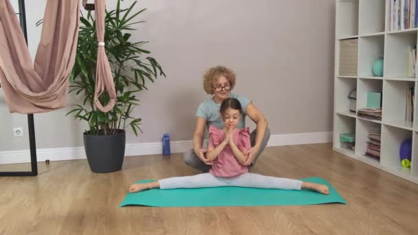 Bestemor og en liten jente sitter på en blå matte og gjør øvelser. – stockvideo