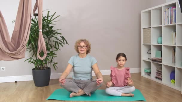 La abuela y un poco están sentados en una alfombra azul y meditando. — Vídeo de stock