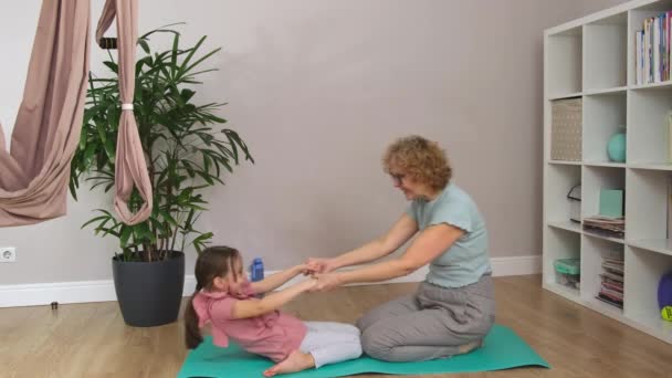 Grandma and a little are sitting on a blue mat doing exercises and hugging. — Stock Video