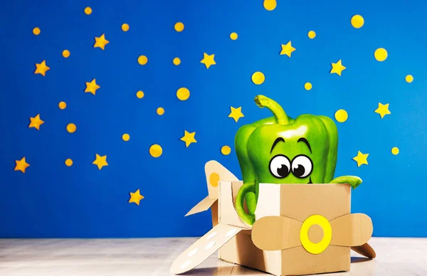 Green pepper in cardboard plane. Green pepper playing in a room. Fun activities. Photo manipulation. Cartoon fresh green pea pod character mascot smiling.