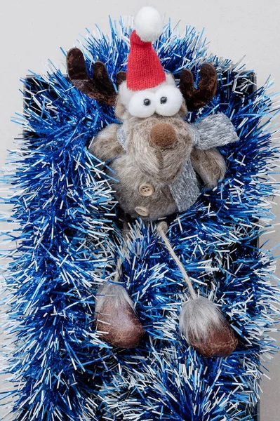 一只带着圣诞帽的可爱的玩具鹿坐在一个盒子里，盒子里镶着蓝色的金银花。圣诞装饰。顶部视图 — 图库照片