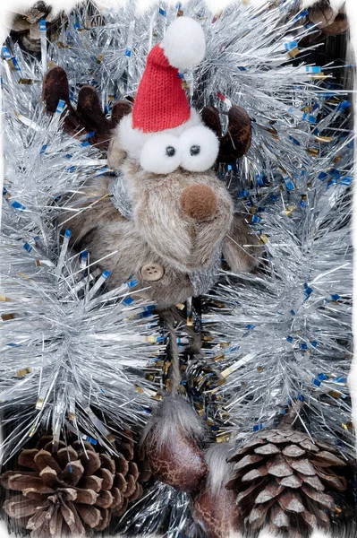 一只长着鼓鼓的眼睛的有趣的小玩具鹿躺在银白色的、有冷杉球果的金银财宝里。圣诞装饰. — 图库照片
