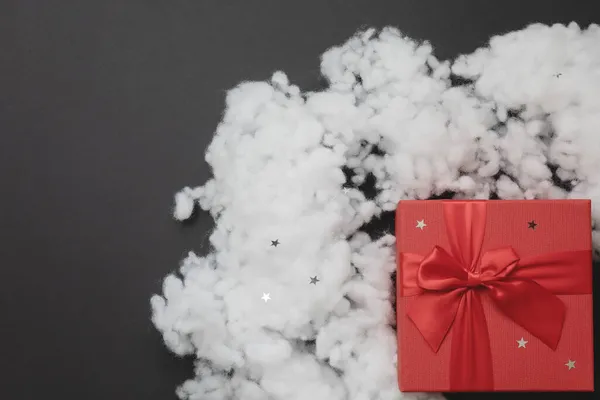 Rode doos met een strik en kunstmatige fiberfil sneeuw op een donkergrijze achtergrond. Kerstmockup. Bovenaanzicht — Stockfoto