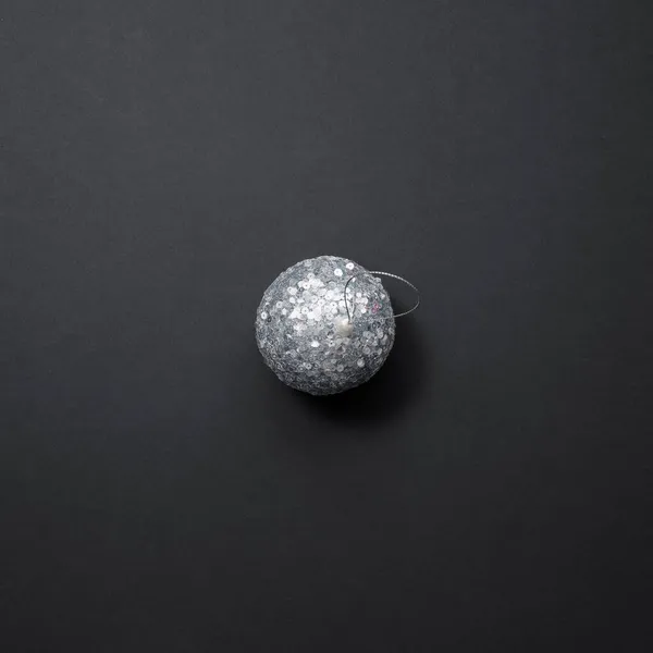 Błyszcząca srebrna kula choinkowa pokryta cekinami leży na czarnym tle. Wystrój świąteczny — Zdjęcie stockowe