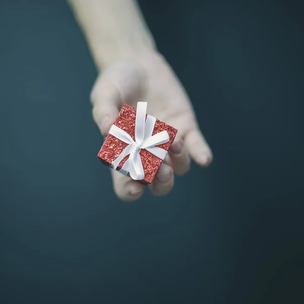 Een kleine glimmende rode doos met een witte strik ligt in vrouwenvingers — Stockfoto