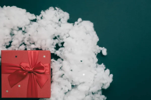 Rode doos met een strik en kunstmatige fiberfill sneeuw met kleine sterren op een smaragdgroene achtergrond. Kerstmockup. Bovenaanzicht — Stockfoto