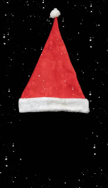 Sombrero de terciopelo rojo de santa claus sobre un fondo negro con granos voladores de nieve alrededor. Maqueta de Navidad — Foto de Stock