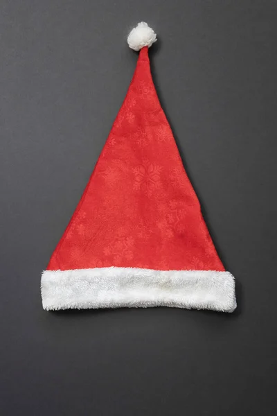 白いバボと縁と暗い灰色の背景に雪片の形でパターンを持つ赤いサンタクラスの帽子。トップ表示 — ストック写真