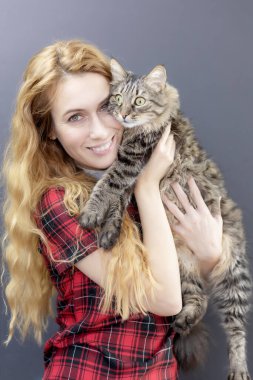 Neşeli bir bayan sürpriz bir tekir kediyi kollarında tutuyor. Kedileri severim.