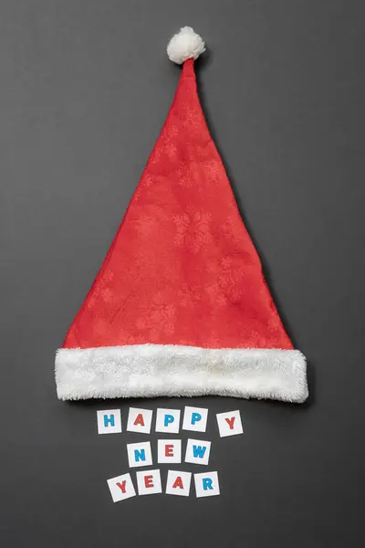 Rot-weißer Weihnachtsmann-Hut und frohes neues Jahr Schriftzug auf grauem mattem Hintergrund — Stockfoto