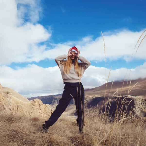 The girl in Santa Claus hat. Made a gesture with her hands funny glasses. Against the backdrop of beautiful nature.