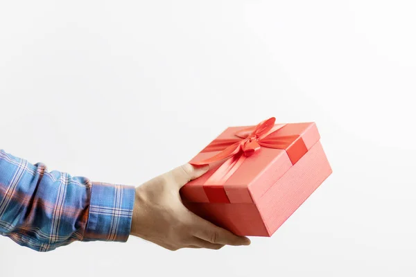 Een mans hand in een geruite mouw houdt een rode doos met een geschenk op een witte achtergrond. Cadeau voor een feest — Stockfoto