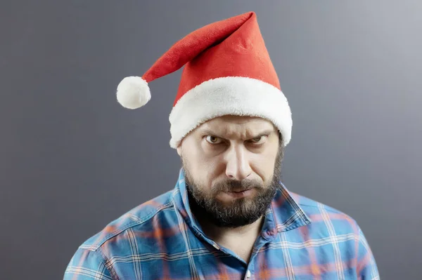 Um homem barbudo de chapéu de Pai Natal e uma camisa de xadrez franziram as sobrancelhas. Papai Noel irritado — Fotografia de Stock