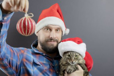 Sakallı bir adam ve Noel Baba şapkalı bir kedi, elinde Noel topu olan bir adam. Şenlik kıyafeti. Noel posteri